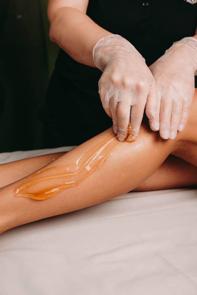 Esthéticienne en gants appliquant de la pâte à sucre ambrée sur une jambe pour l'épilation, en salon de beauté.
