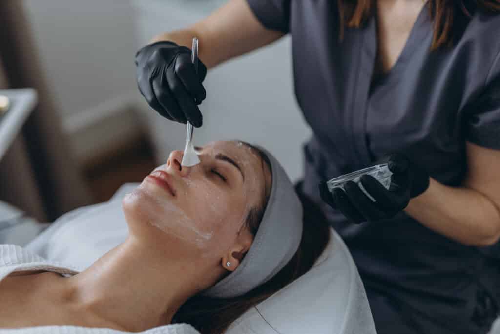 Esthéticienne appliquant un masque facial hydratant avec un pinceau sur le visage d'une femme détendue en institut.